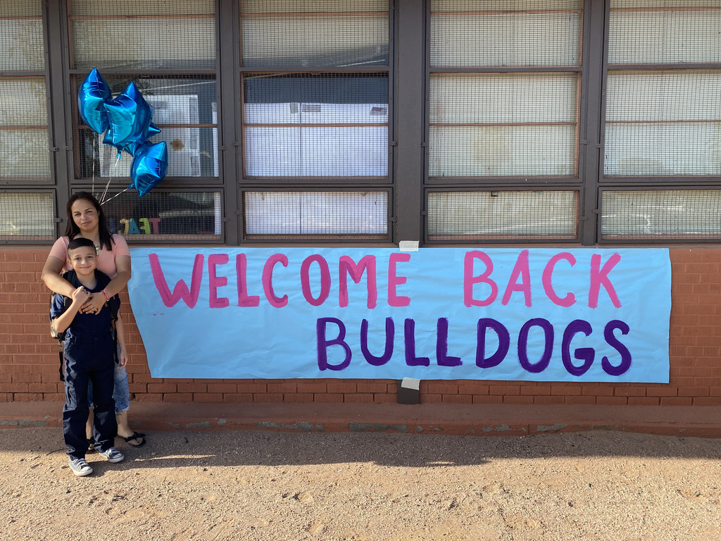 Mother and son standing in front of a welcome back sign outside of the school