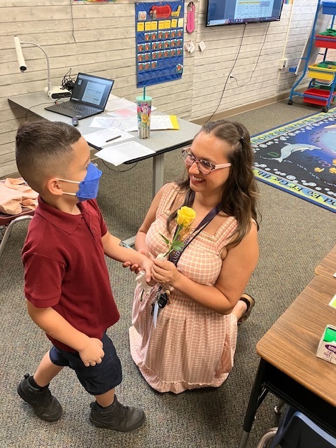 An elementary aged student handing his teacher a yellow rose on the first week of school