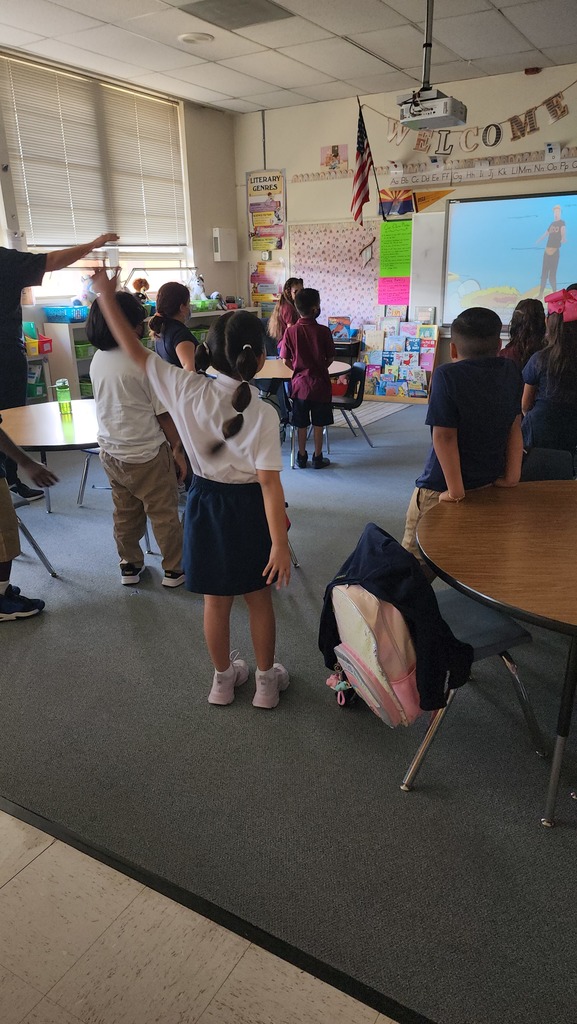 students in a classroom stand up and practice rules by raising their hand