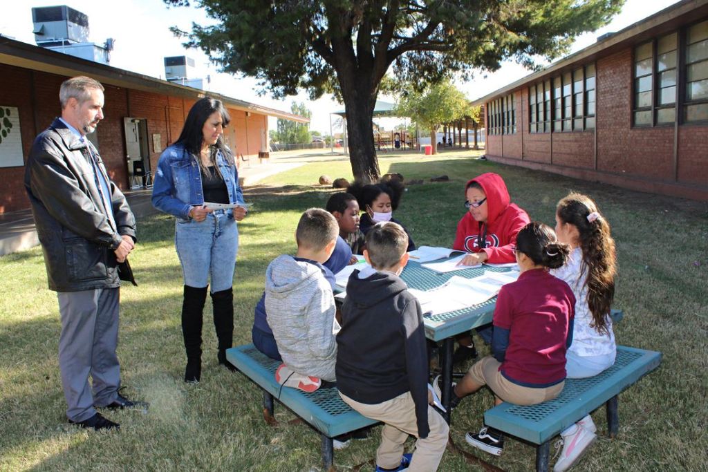 Board president and principal look at students collaborating at a picnic table.