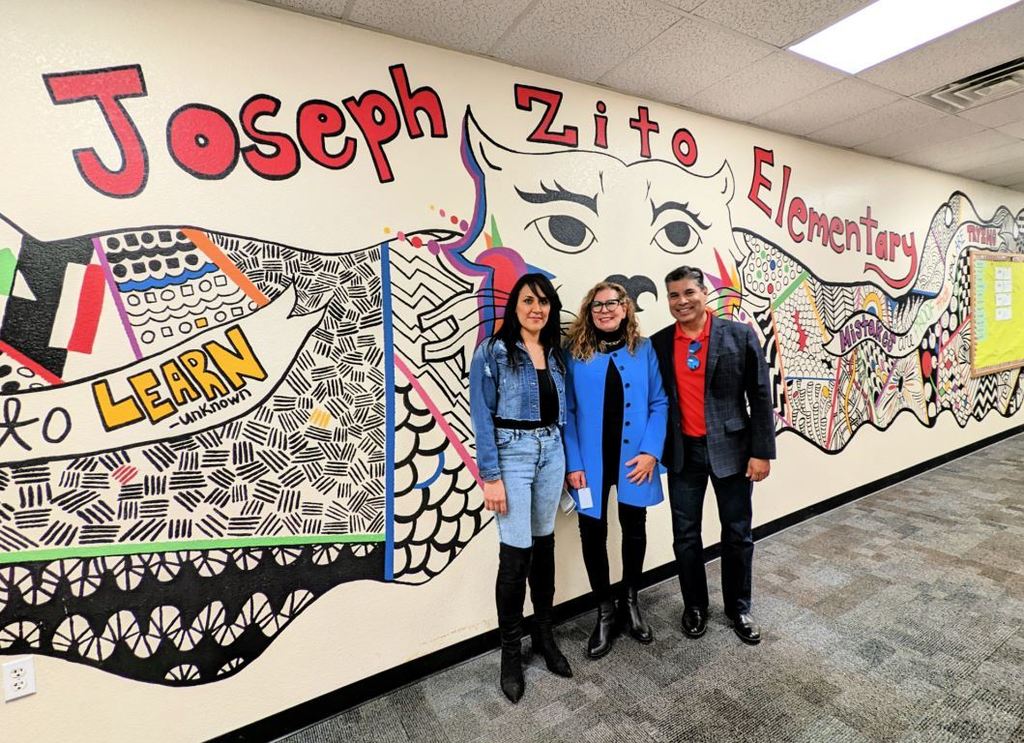 Board president, principal, and superintendent standing in front of a mural.