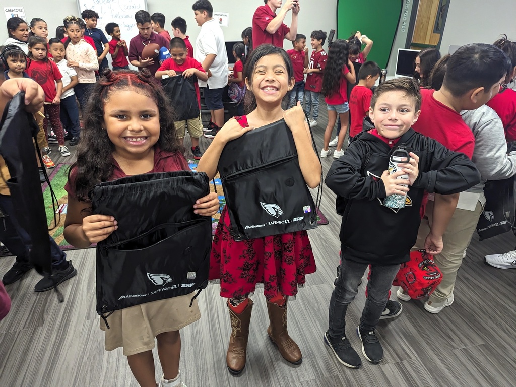 Students smiling with their autographed backpack from the Arizona Cardinals
